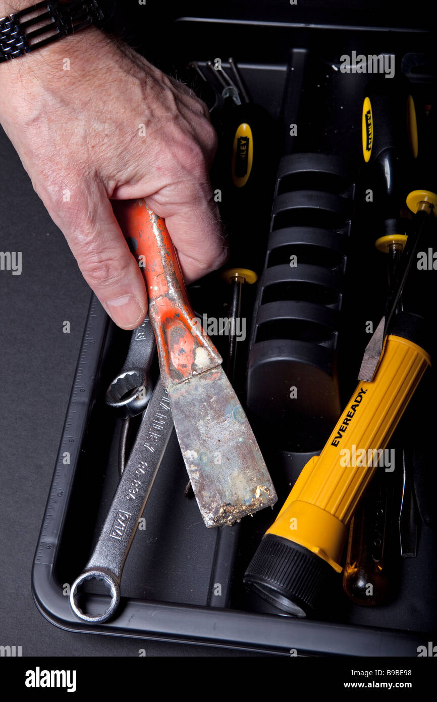A repairman takes a putty knife from a toolbox full of tools. Stock Photo