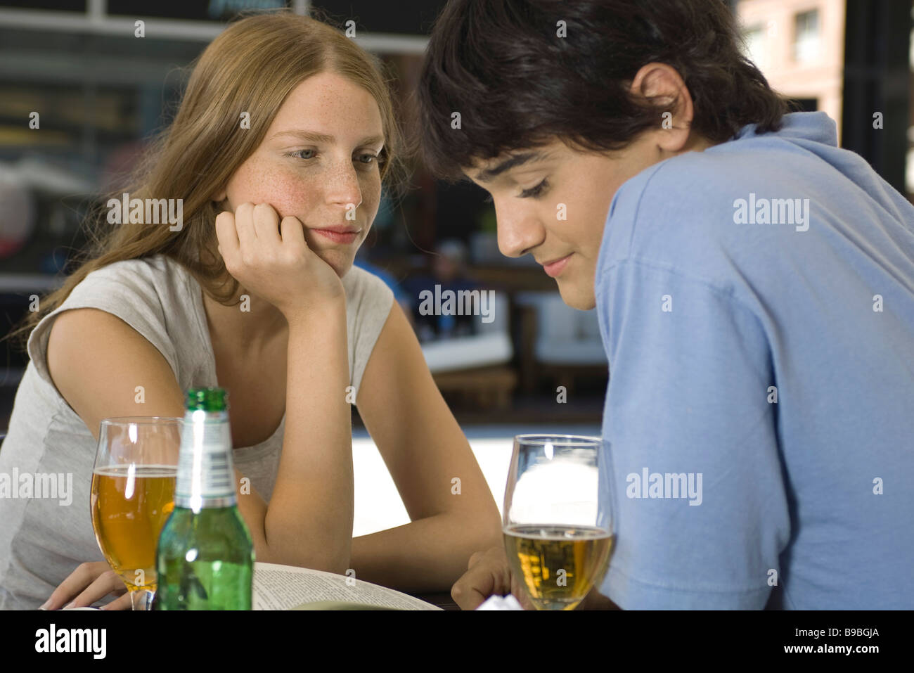 Young couple sitting at outdoor cafe, looking down at book Stock Photo