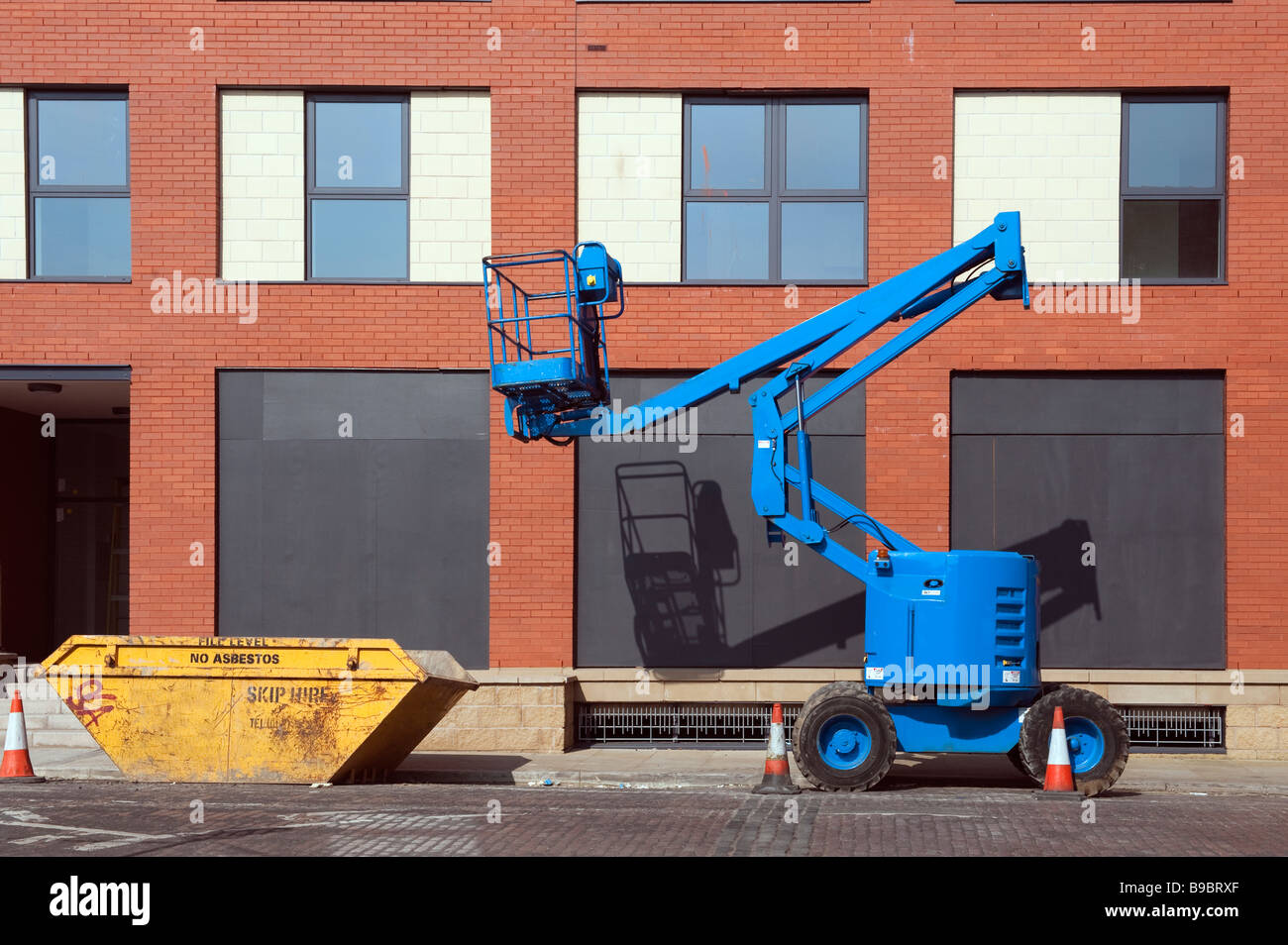 Blue mobile crane and a yellow hire skip against a new red brick building Stock Photo