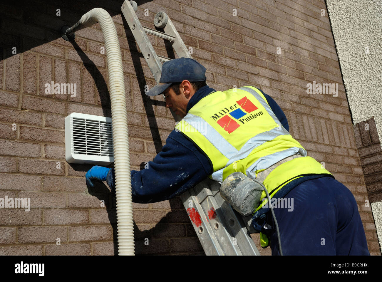 Worker plugging a hole where recycled glass fibre insulation has been blown into the wall cavity Stock Photo