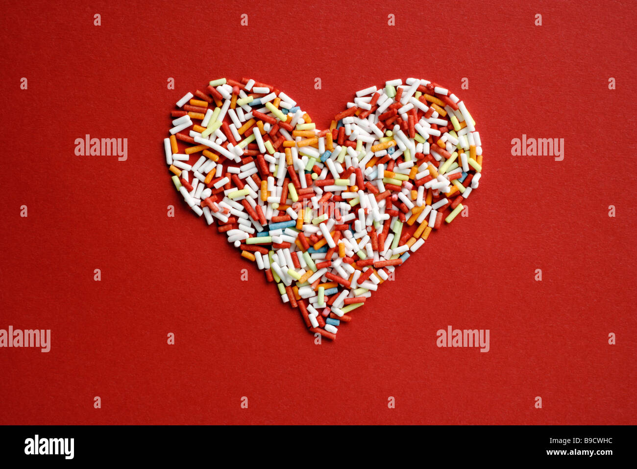 Herz aus farbigen Zuckerstreusel auf roten Untergrund Stock Photo