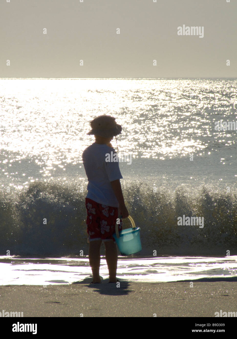 boy on beach with bucked playing near ocean waves Stock Photo