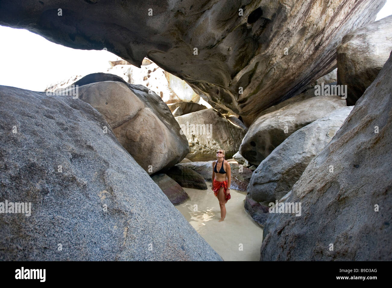 A woman walks amongst the huge boulders inside The Baths at Virgin Gorda BVI Stock Photo