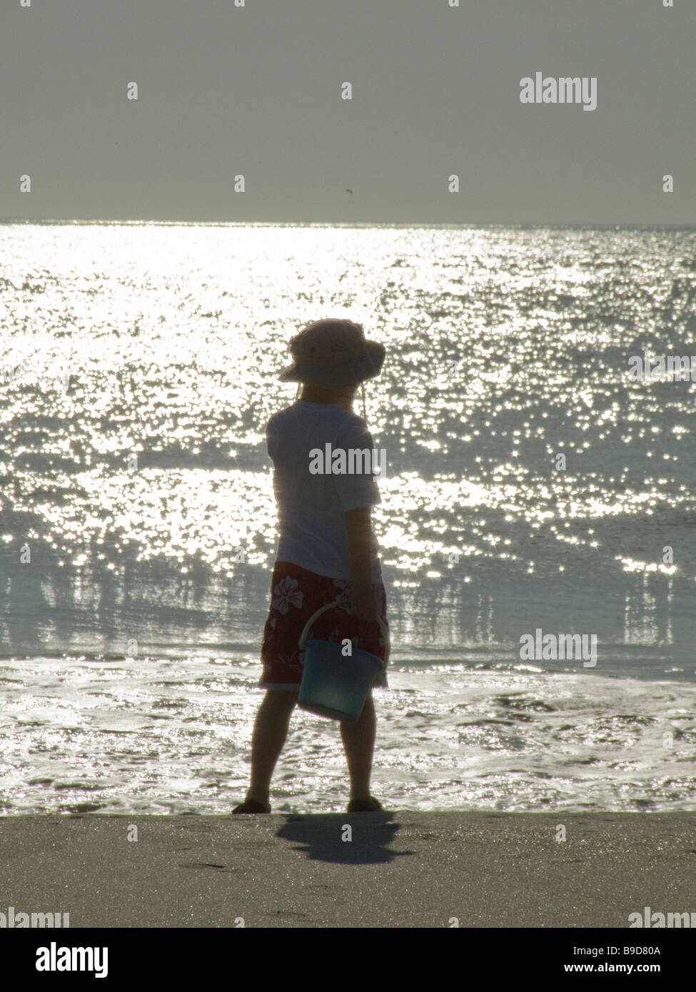 boy on beach with bucked playing near ocean waves Stock Photo