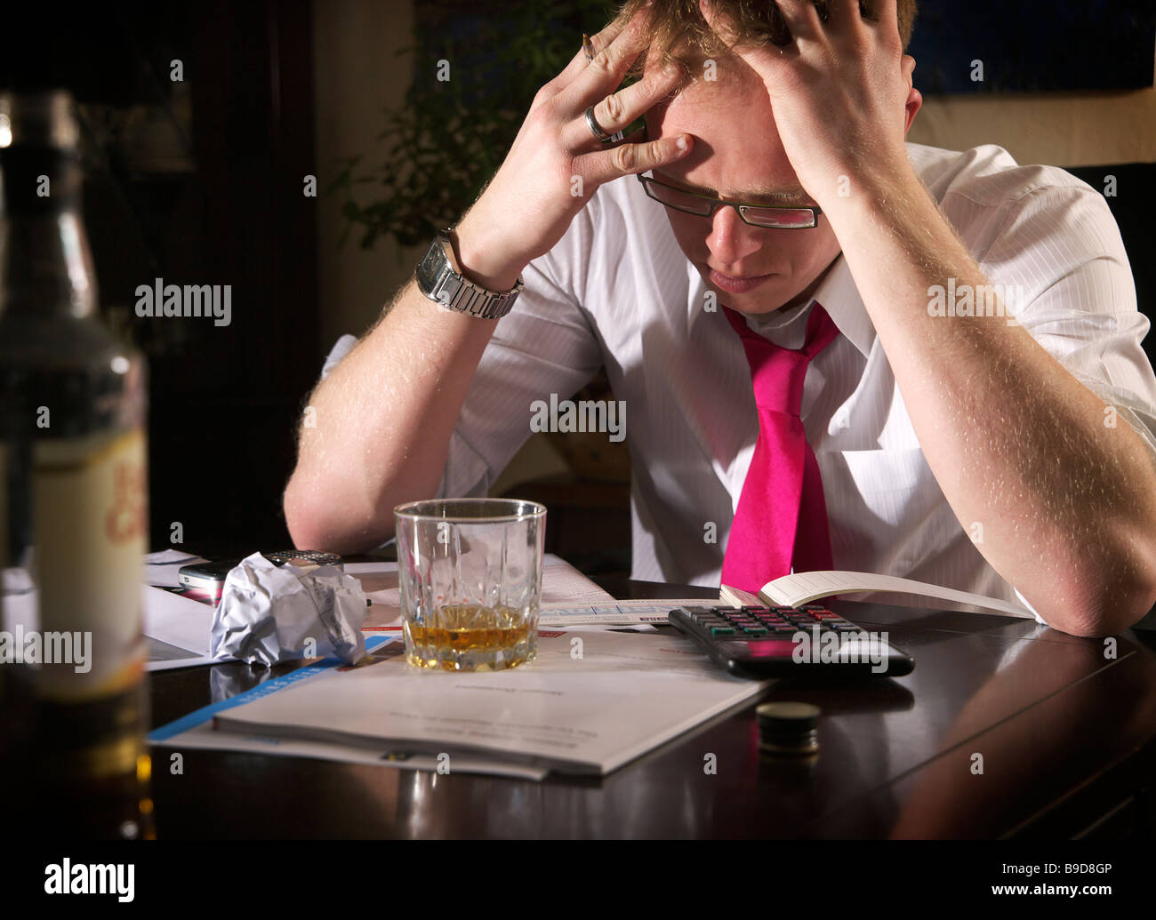 Young male struggling to work finances out and sipping whisky to ease the pain Stock Photo