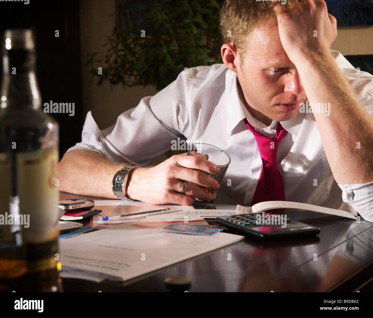 Young male struggling to work finances out and sipping whisky to ease the pain Stock Photo