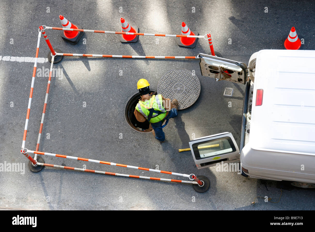 Maintenance utility worker looks into open manhole on the street. Stock Photo
