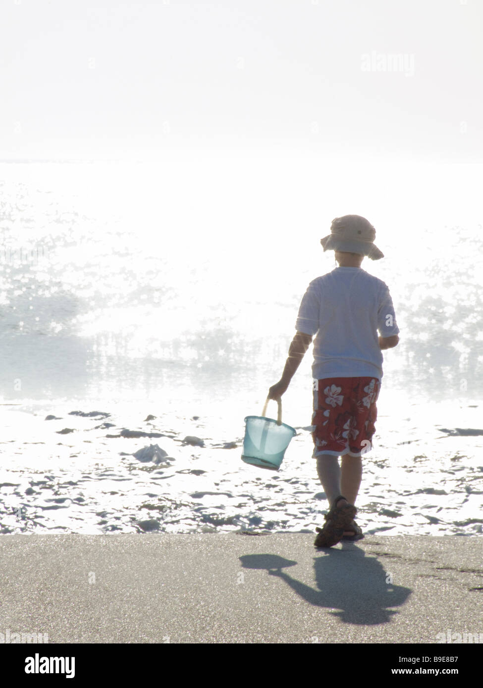 boy on beach with bucked playing near ocean waves Stock Photo