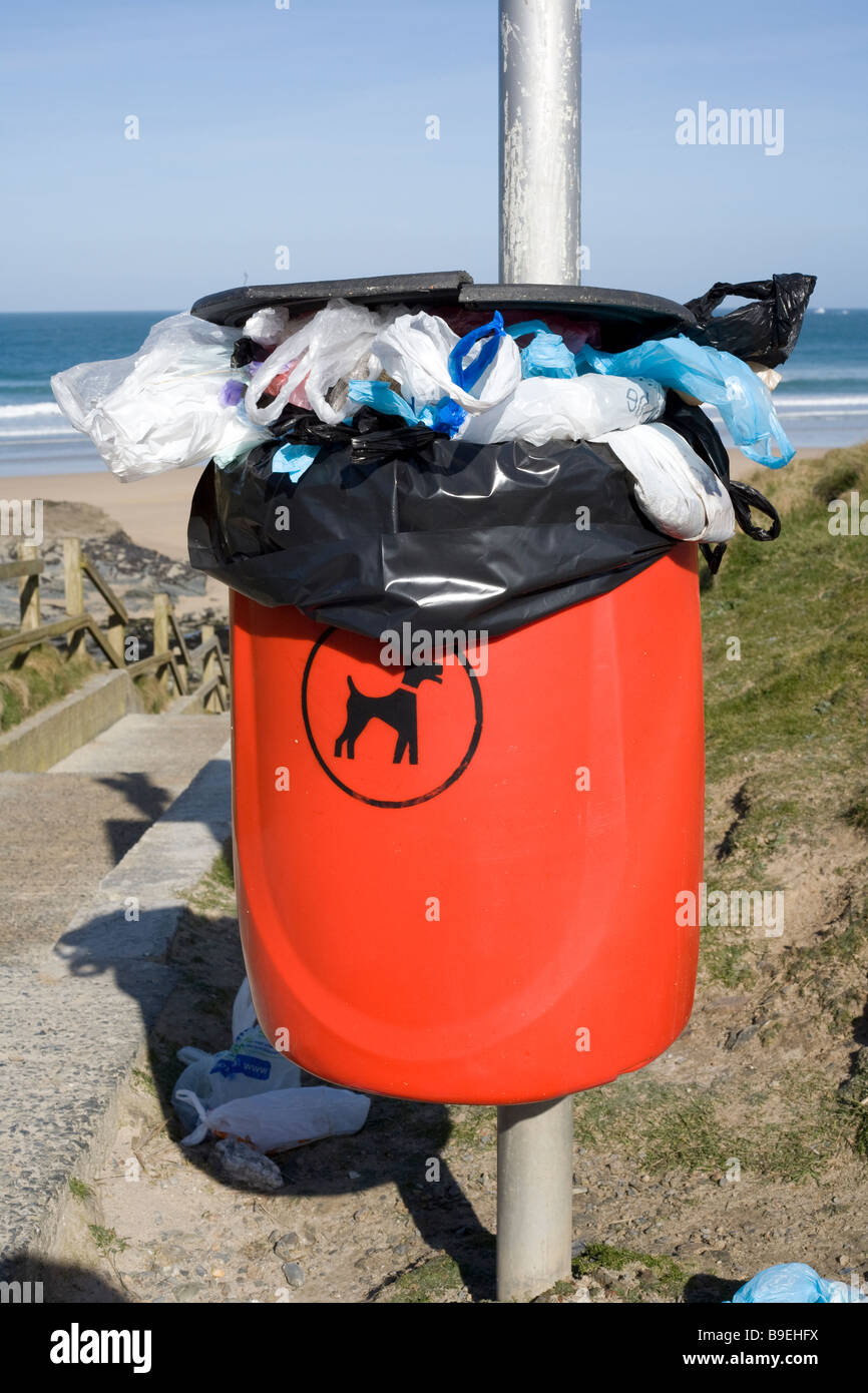 Red dog waste bin full and overflowing with bags, near a British beach. Stock Photo