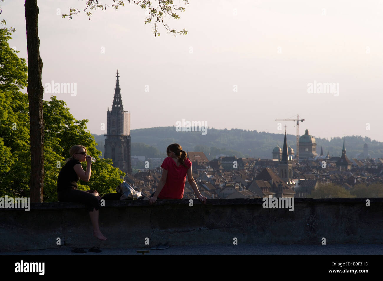 Two young women sitting on a wall while enjoying view over Old Town Rosengarten Berne Canton of Berne Switzerland Stock Photo