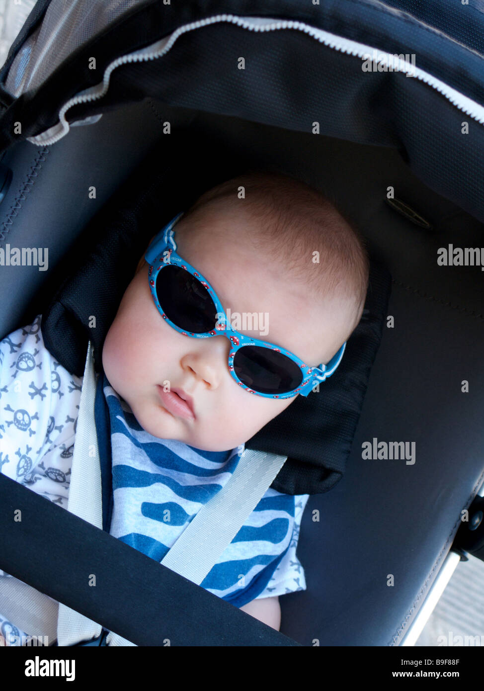 Young male child in a pram buggy wearing sunglasses dressed in blue angled Stock Photo