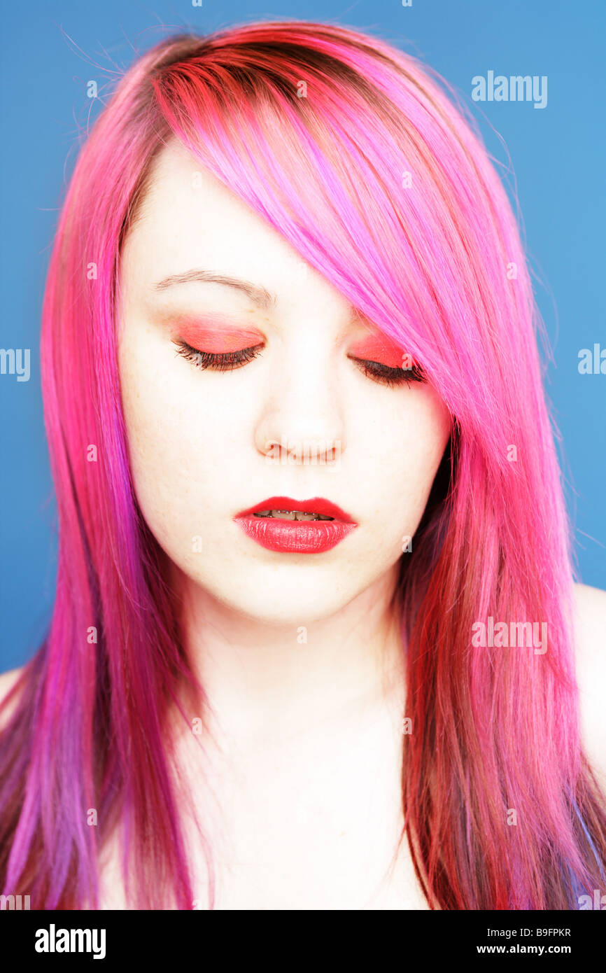 Young teen with bright pink hair red lips and eye shadow looking down to the ground. Stock Photo