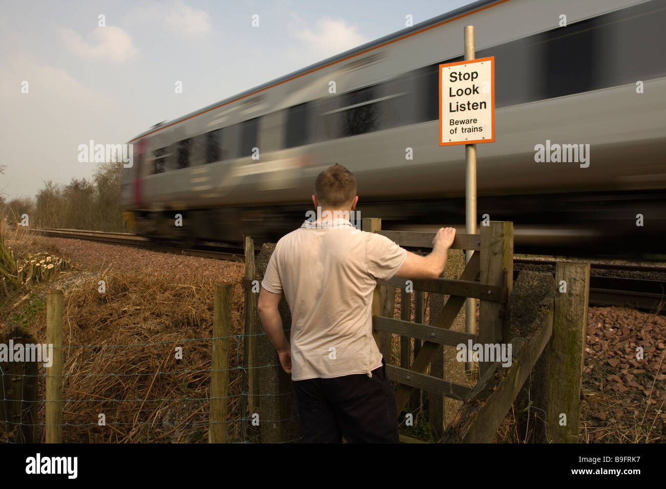 A train passes whilst a person waites to cross a railway track Stock Photo