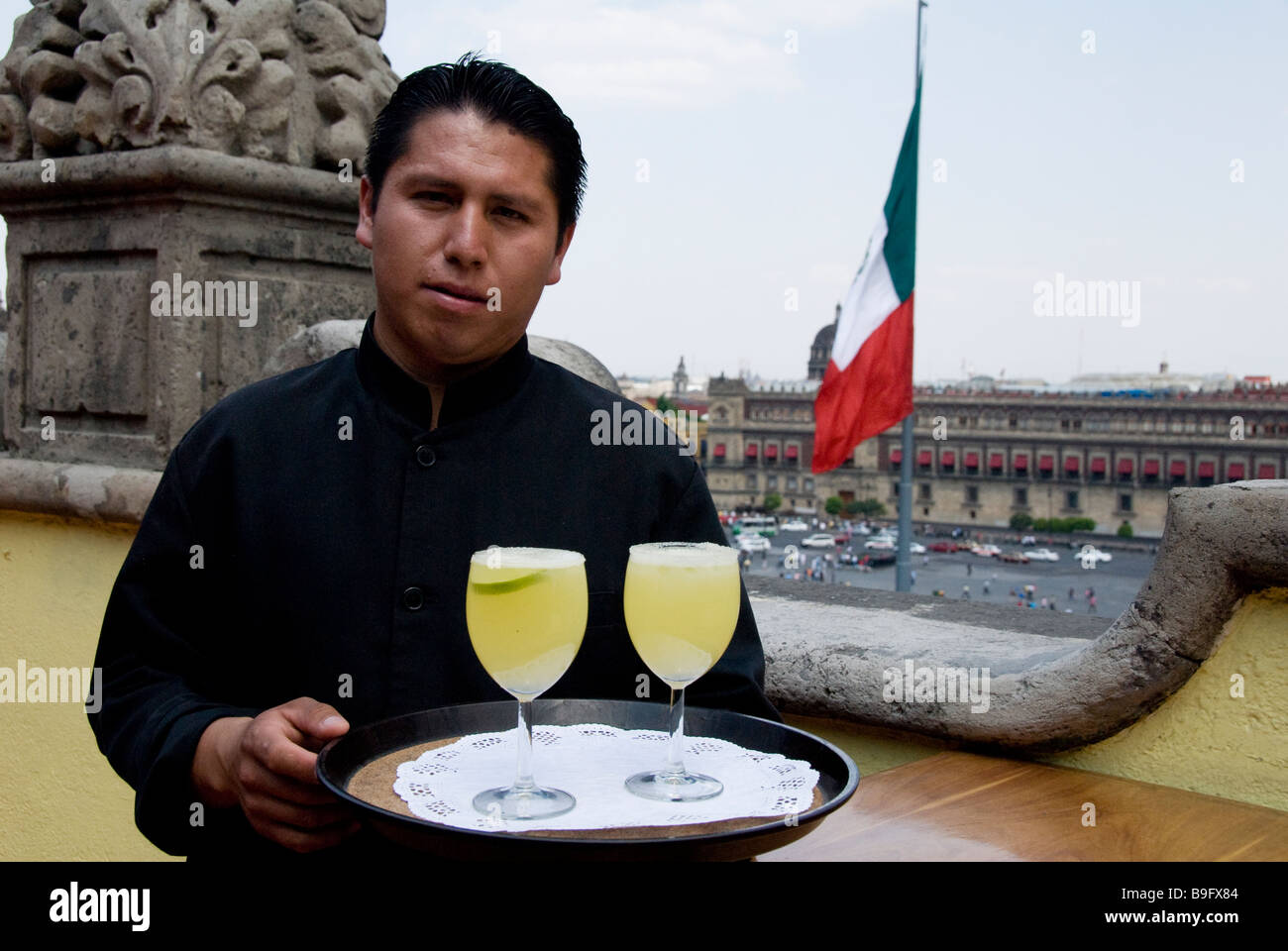 a mexican waiter serving margarita with a view on Plaza de la Constitución and mexican flag, Mexico city, Mexico Stock Photo