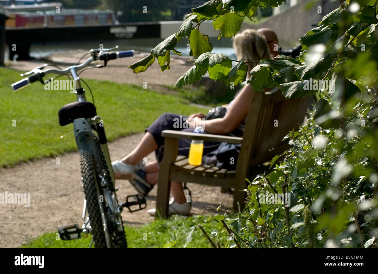 Couple sat on bench on summers day with bike in foreground Stock Photo