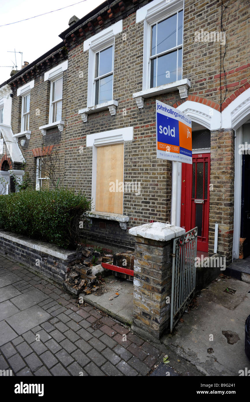 A sold sign stands before an empty, possibly repossessed, flat, maisonette with boarded windows in London Stock Photo