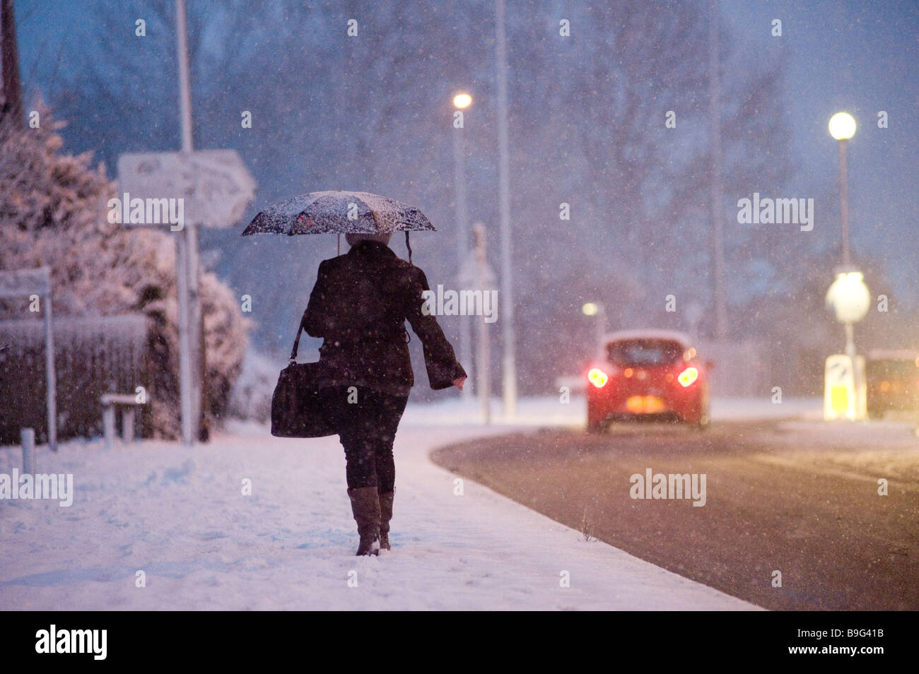 Lady walking home from work along a snow covered pavement on a winters evening in england Stock Photo