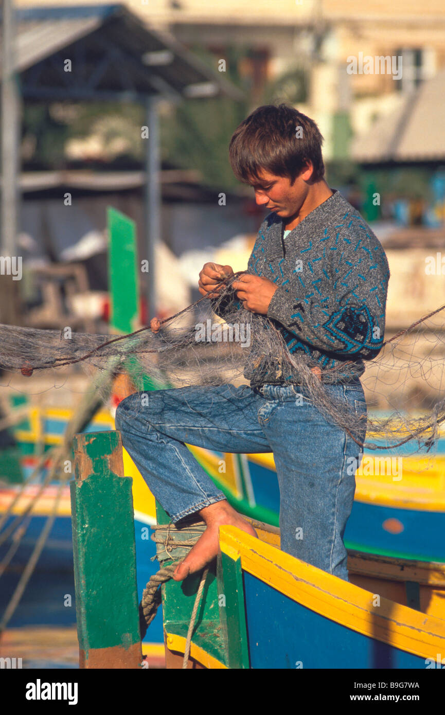 A boy mends fishing nets on luzzu class fishing boat Marsaxlokk harbour Malta Maltese Islands Mediterranean Sea Stock Photo