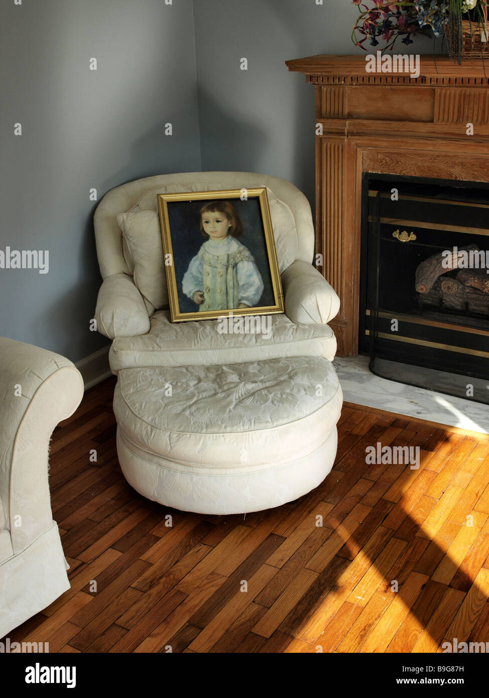 living room scene with white soft chair holding a painting next to fireplace mantel on wooden floor Stock Photo