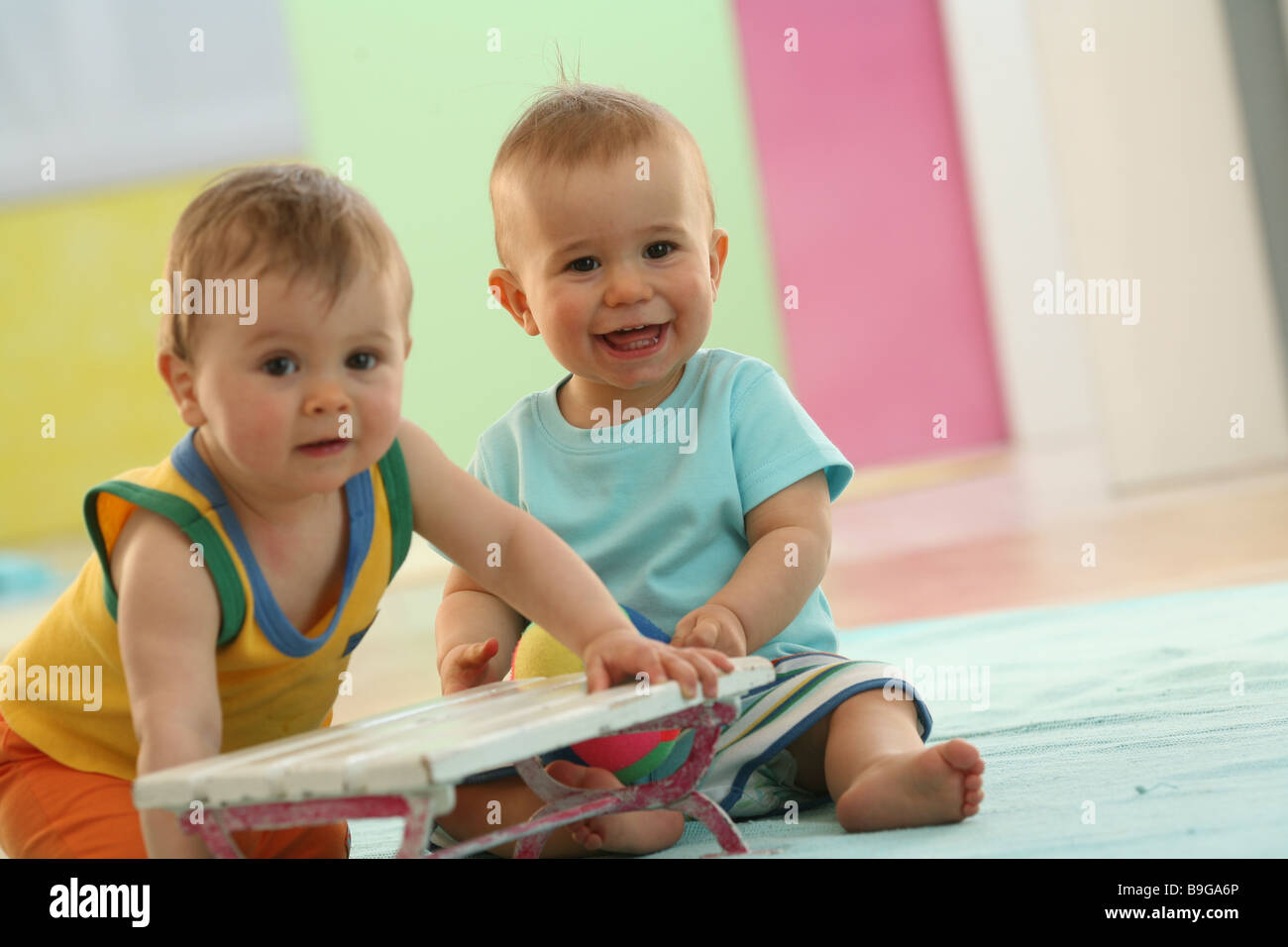 Babies sitting side by side plays smiling friends  10 months wakened alertly babies employing gaze camera development exploring Stock Photo