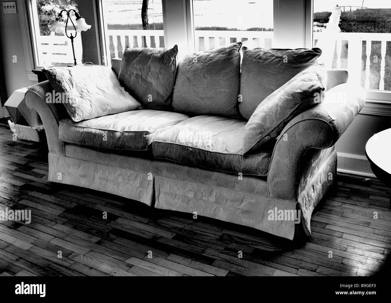 living room lounge couch or sofa in black and white with bright sun on furniture and wooden floor with background fence Stock Photo
