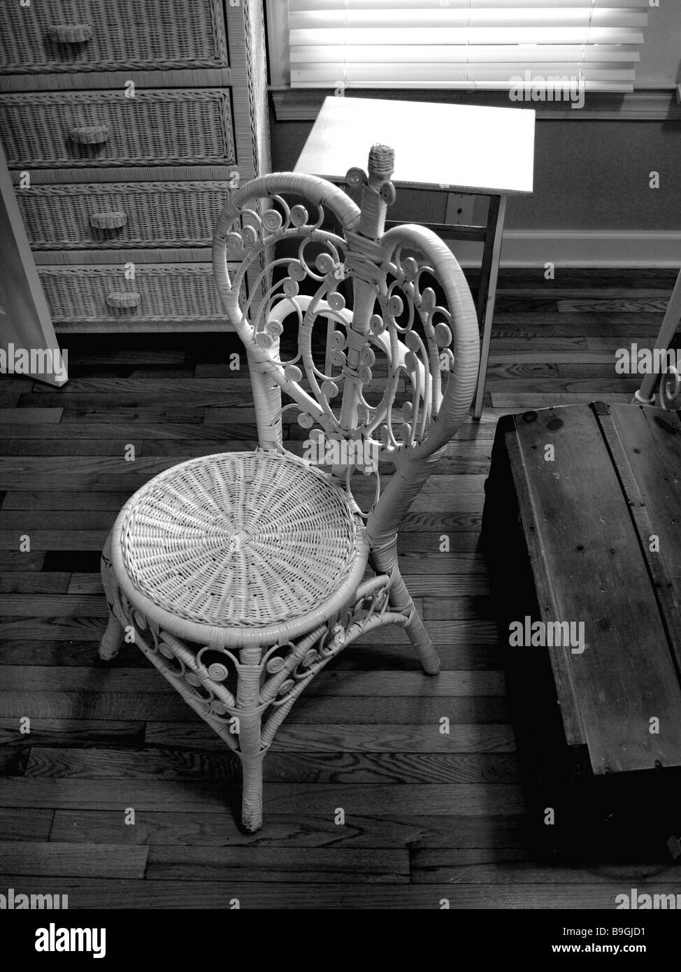 wicker chair in room with wooden floor with wicker chest of drawers cabinet and trunk box in black and white Stock Photo
