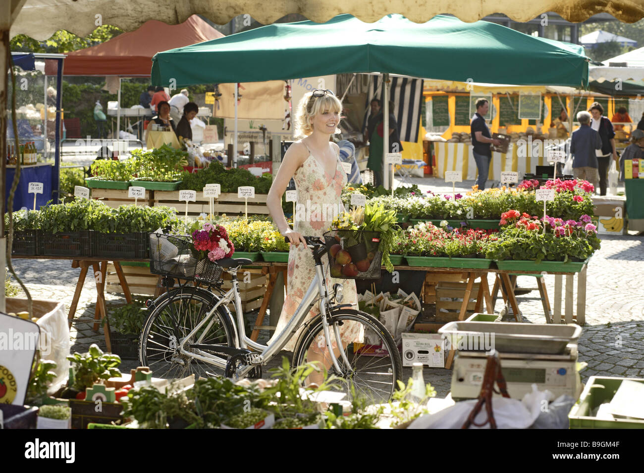 Week-market woman bicycle basket detail buys series people customer blond summer-dress wheel purchase-basket vegetables herbs Stock Photo