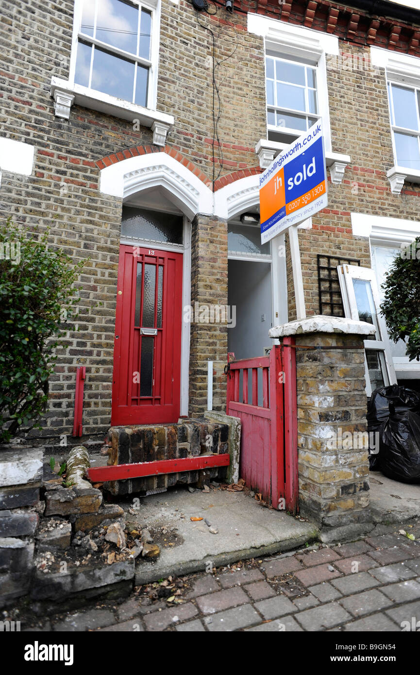 A sold sign stands before an empty, possibly repossessed, flat, maisonette with run-down, blocked entry in London Stock Photo