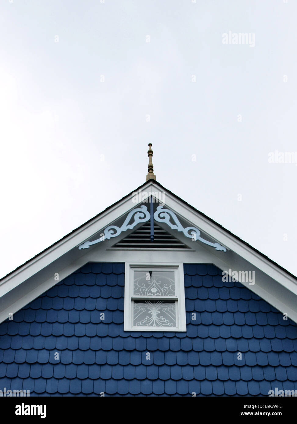 roof peak of house with ornate woodwork blue shingles and window