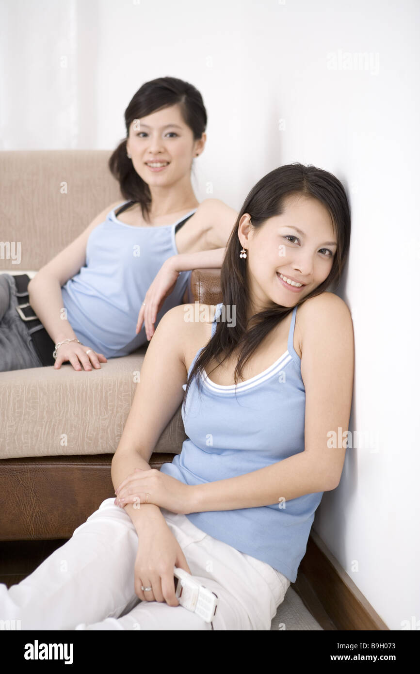Two young women smiling one leaning on wall another on sofa portrait Stock Photo