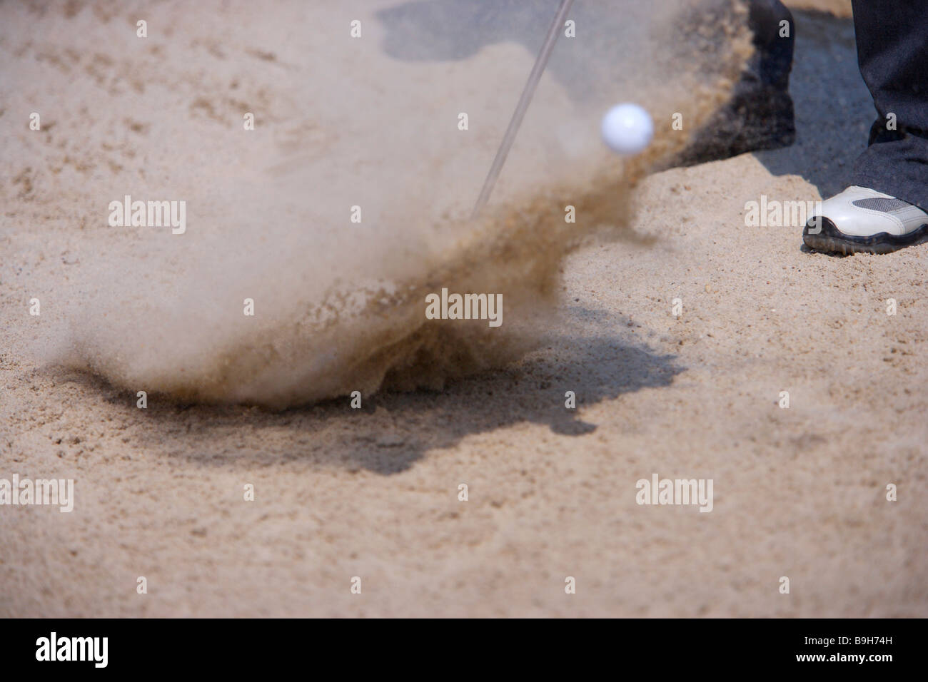 Man hitting golf ball out of sand trap low section blurred motion Stock