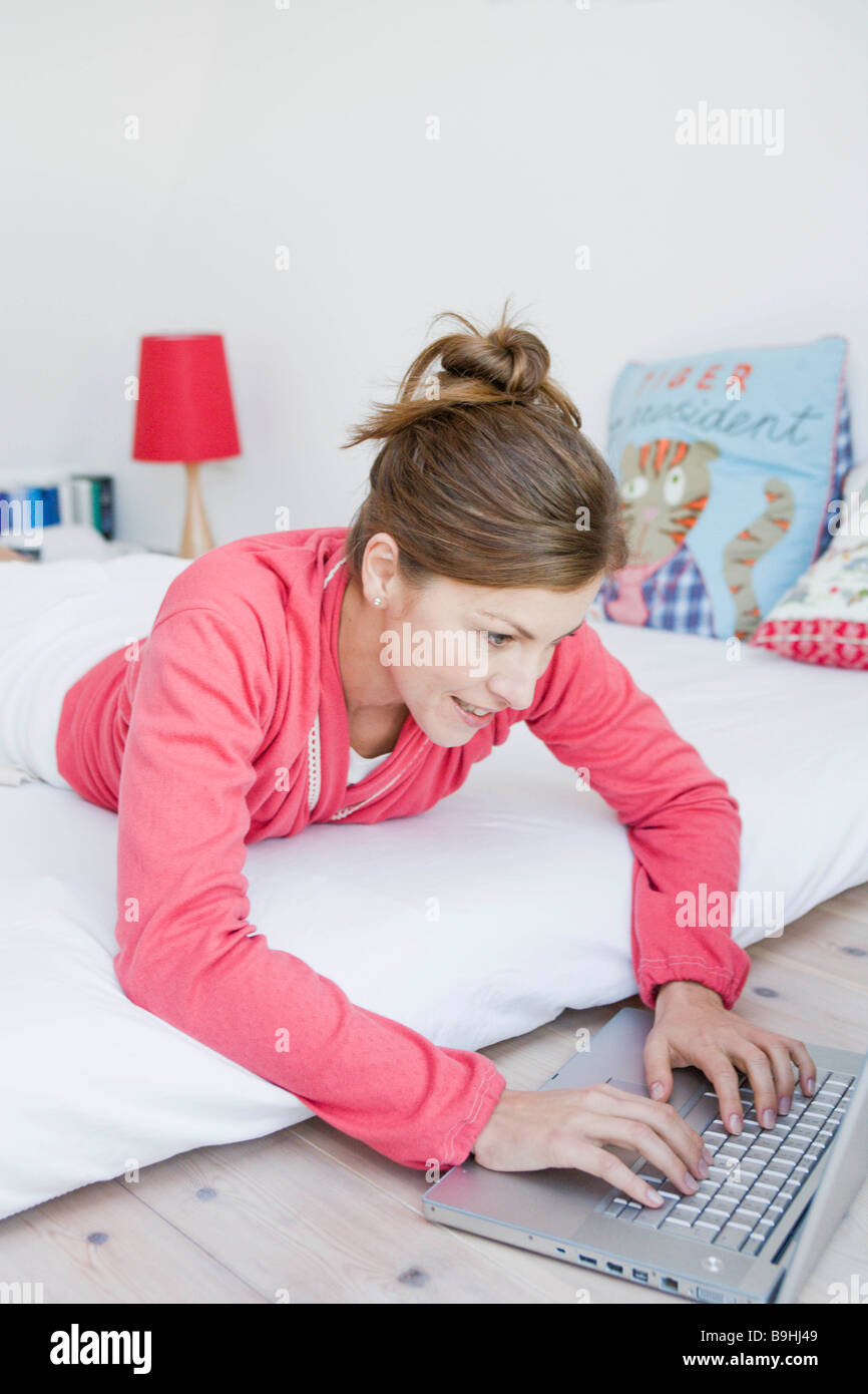 Woman lying on bed with laptop Stock Photo - Alamy