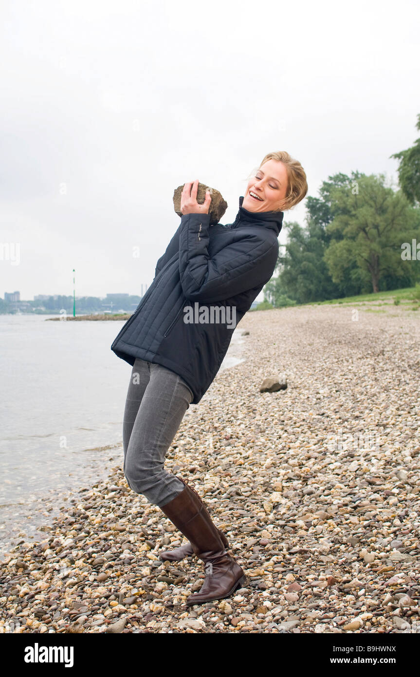 Woman on the bank of a river, lifting a stone Stock Photo