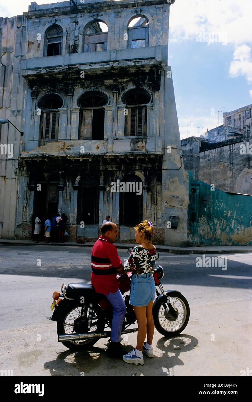 Woman talking to a man on a motorbike, streetscene in front of house ruins, San Lazaro, Centro Habana, Havana, Cuba, Caribbean Stock Photo