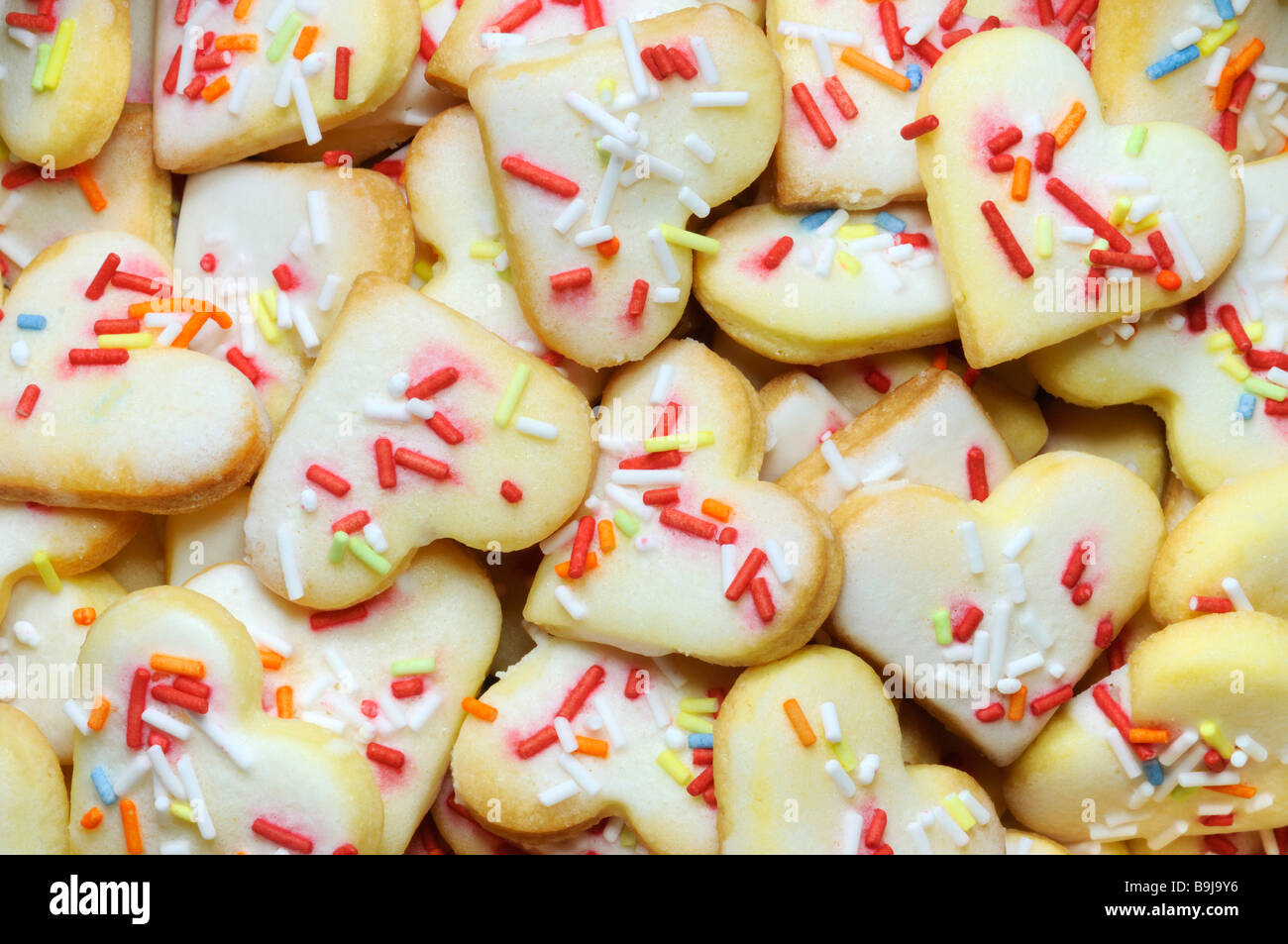 Heart-shaped short pastry biscuits with multicoloured sugar sprinkles, filling the picture Stock Photo