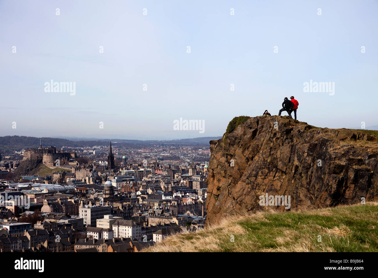 Three males on the top of Salisbury Crags, Holyrood park, Edinburgh, Scotland, UK, Europe, with the city in the background Stock Photo