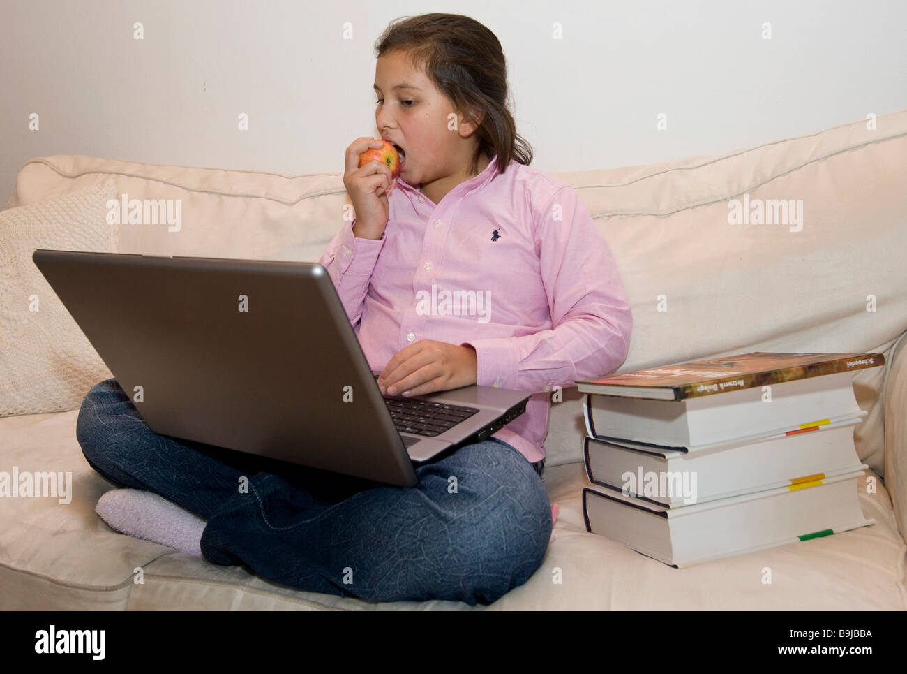 Student, approx. 11 years old, working on a laptop while eating an apple Stock Photo