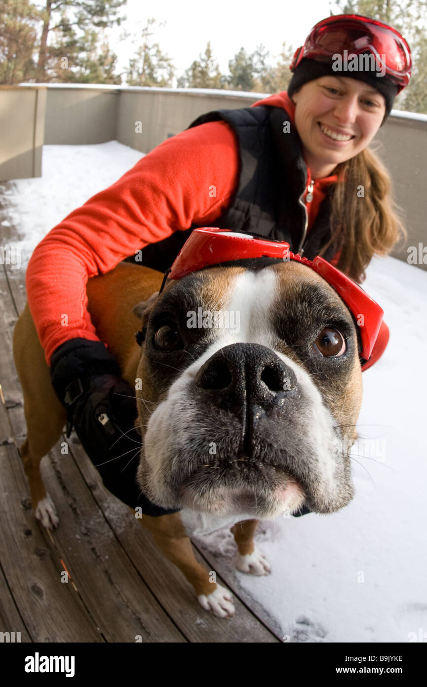Close up of a young woman and a boxer dog wearing goggles in the snow