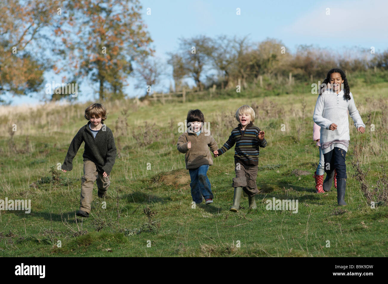 Children running down hill in field Stock Photo