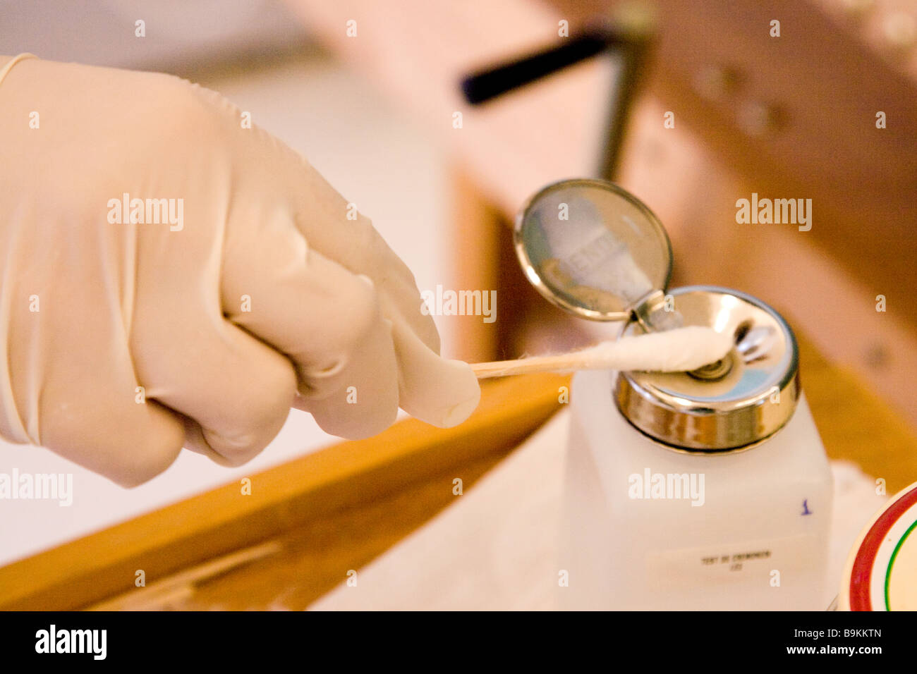 Hand with gloves and a cotton swab taking a porduct from a bottle in a laboratory. Stock Photo