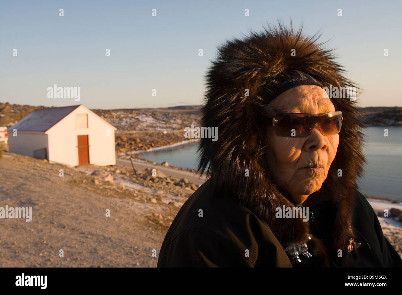 Elderly woman wearing fur hood and sunglasses near coast, Taloyoak inuit settlement Nunavut, Northwest Passage, Canadian arctic, Canada Stock Photo