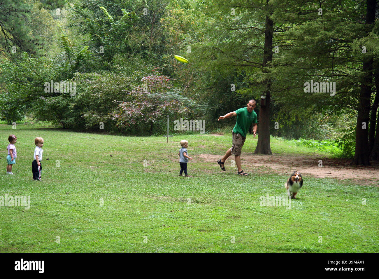 Children watching a young man play frisbee with his dog at the park. Stock Photo