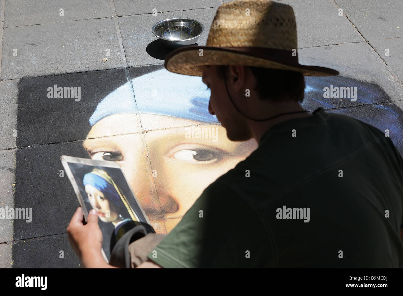 Street artist drawing Girl with a Pearl Earring on pavement. Stock Photo