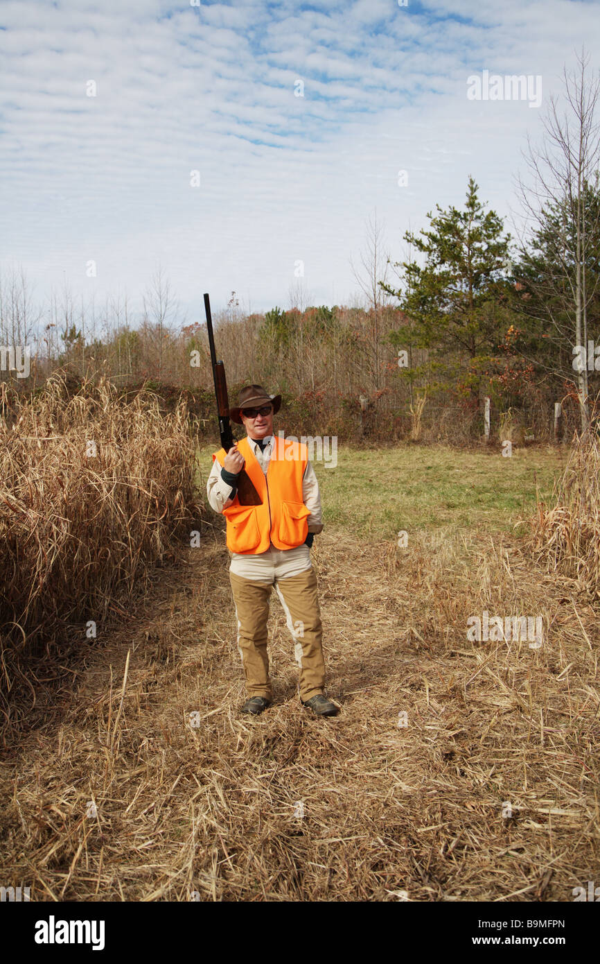 Hunter with orange safety vest holding shotgun in safety position Stock Photo