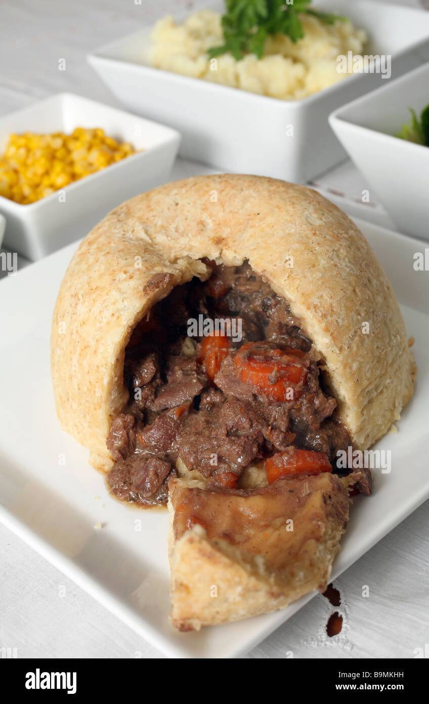 Steak and kidney pudding (with carrot and mushroom) on a buffet with vegetables. Stock Photo