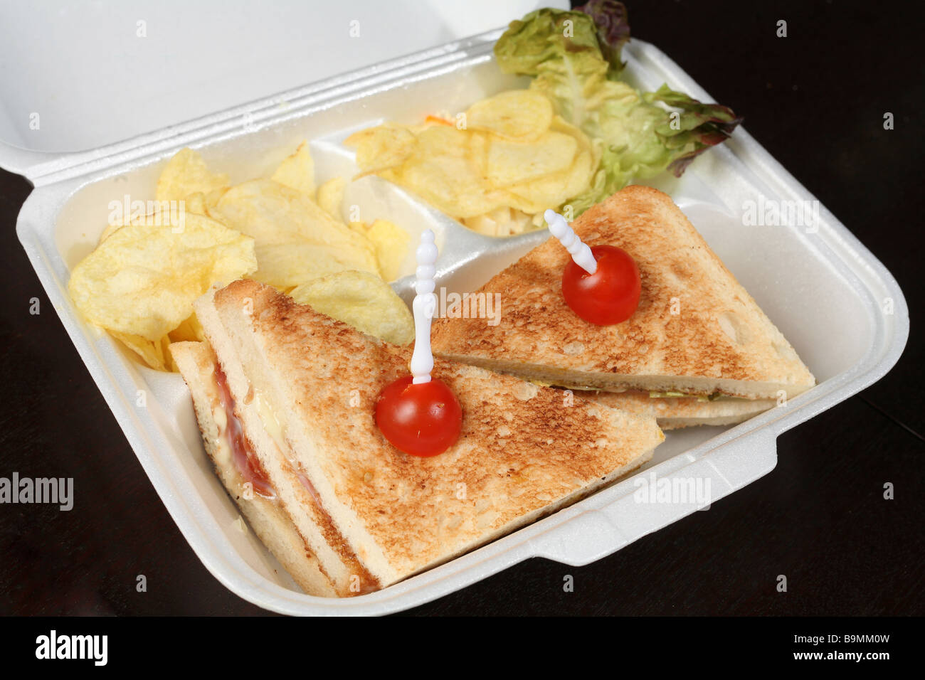 A club sandwich with lettuce and potato chips in a polystyrene box on a