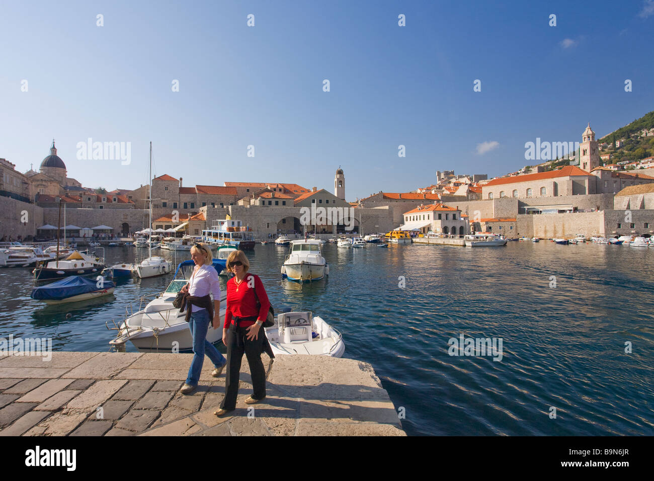 Two women visit old harbour in walled city of Dubrovnik in summer sunshine Dalmatian Coast Croatia Europe Stock Photo
