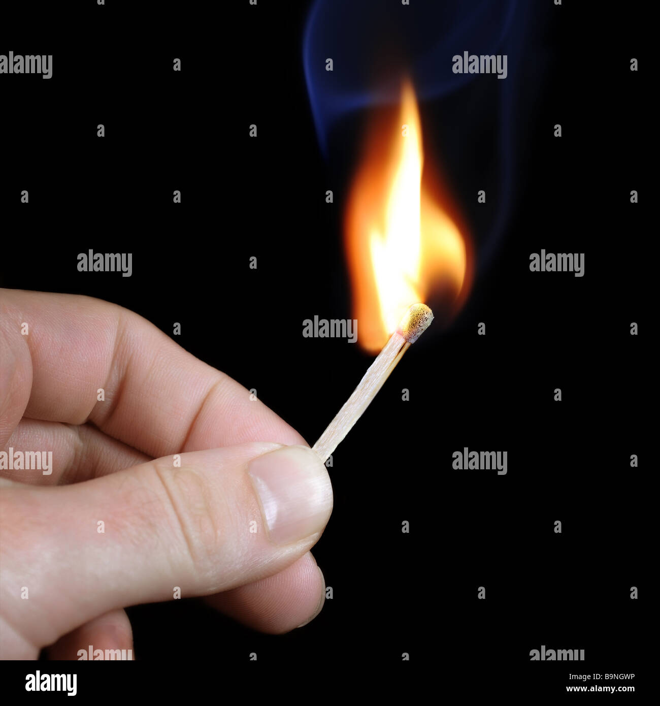 Hand holding a burning match on black background with blue smoke above. Stock Photo
