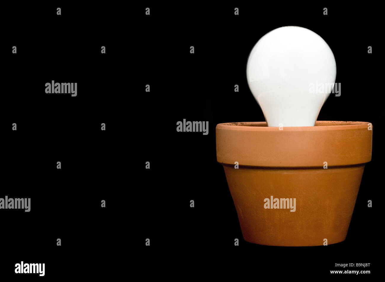 Glowing incandescant bulb in a planter with space for copy on the black background Stock Photo