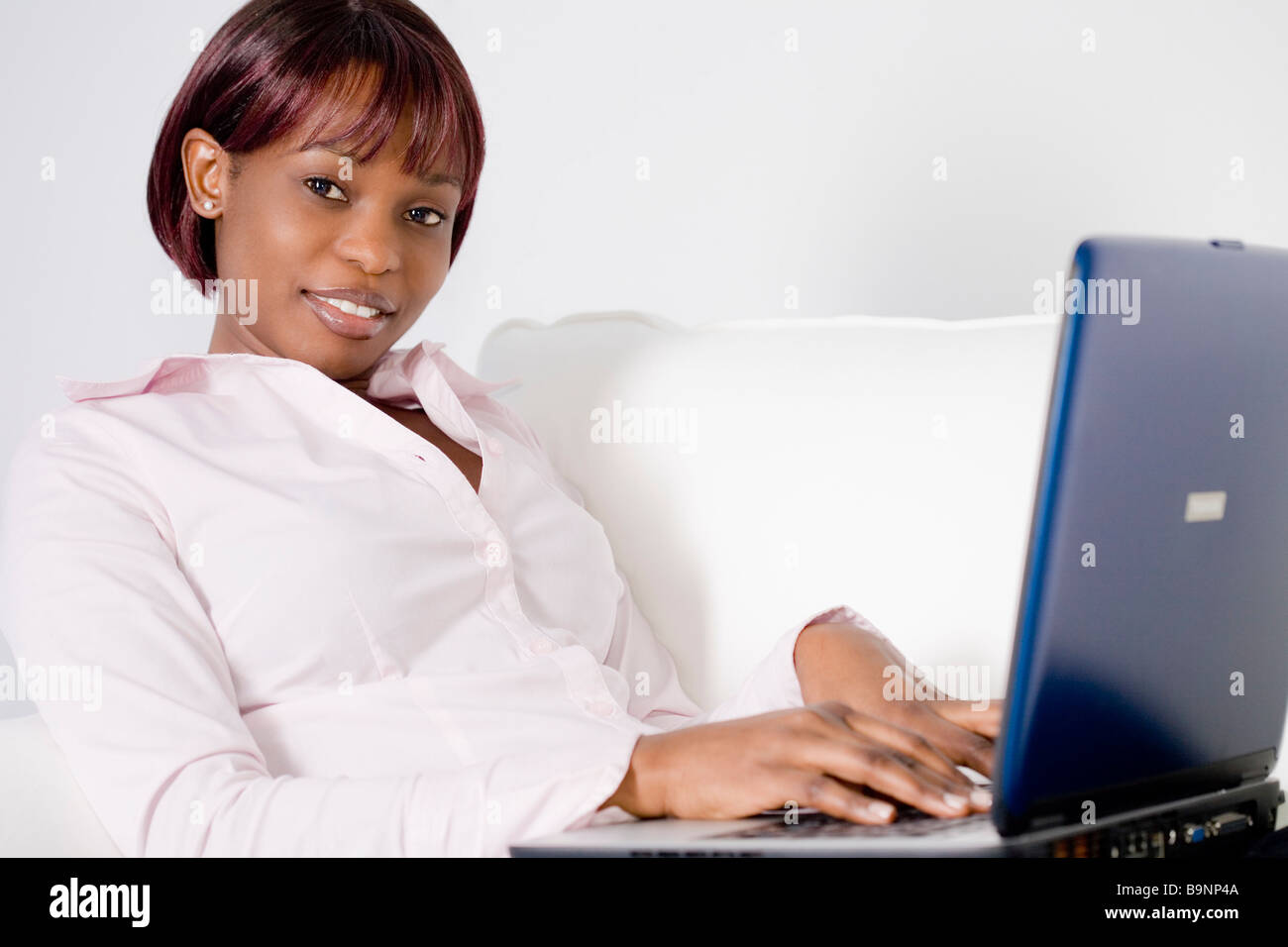portrait of black woman sitting on sofa and working with laptop ...